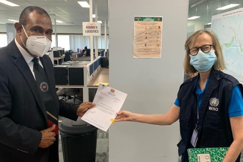 A middle-aged black man in white face mask holds document with shorter white woman with fair hair.