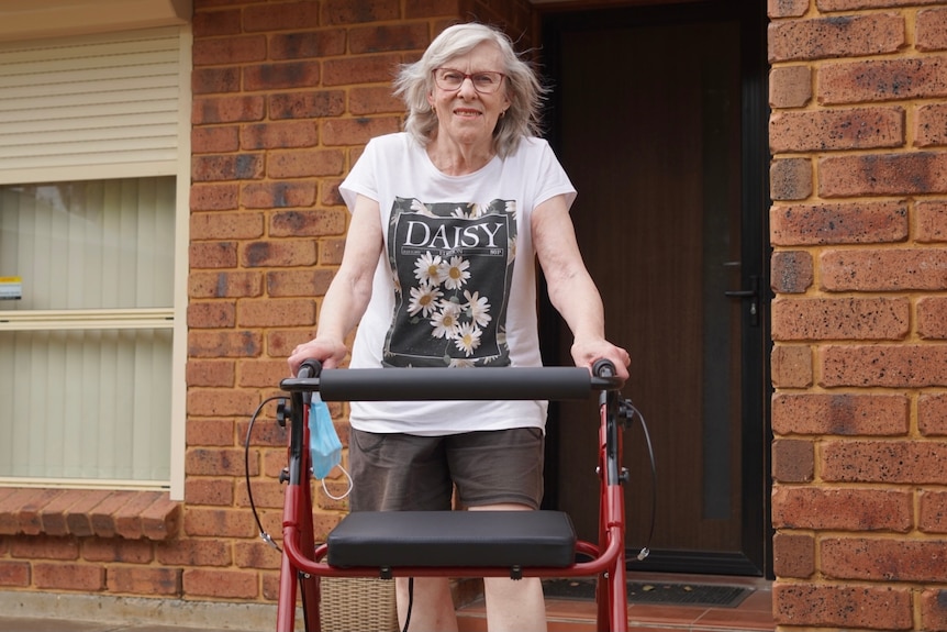 A woman standing with a walking frame in front of a house