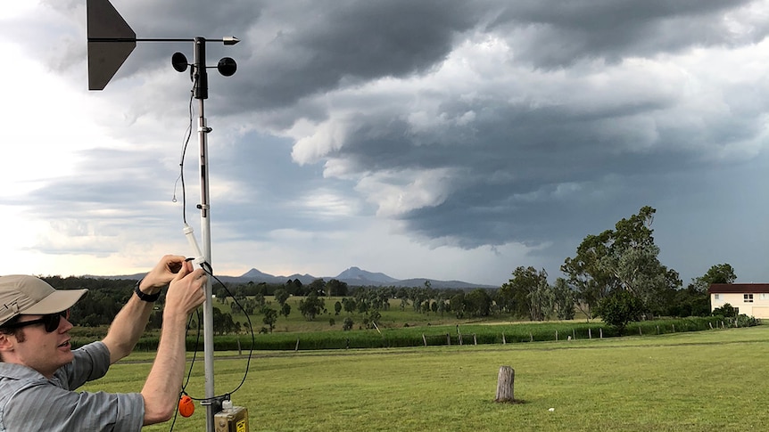 Dr Joshua Soderholm works on weather instruments with storm clouds in distance at Gatton.