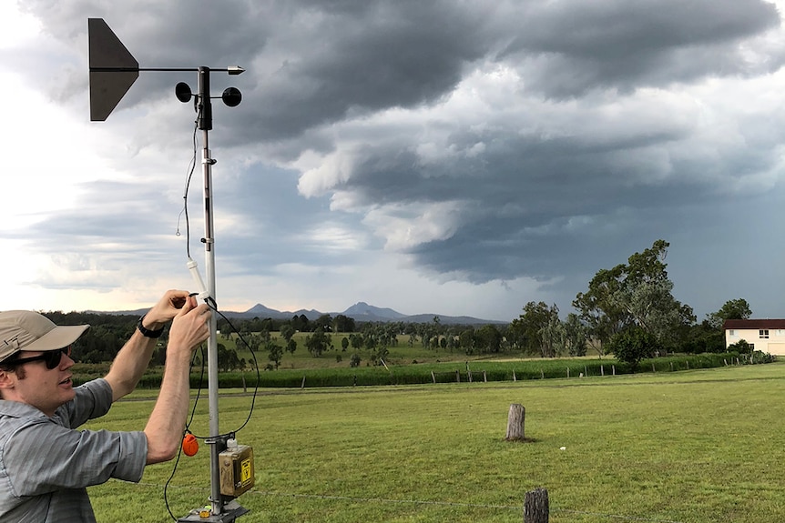 Dr Joshua Soderholm works on weather instruments with storm clouds in distance at Gatton.