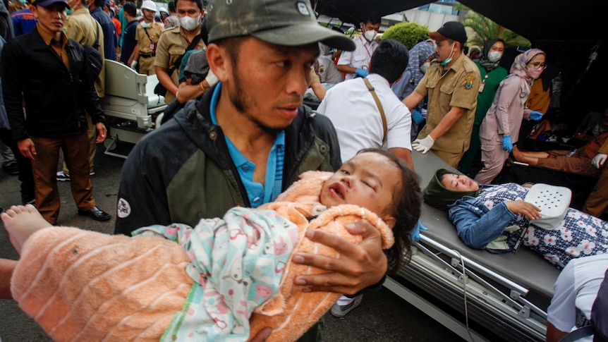 A man carries an injured child to receive treatment at a hospital, after an earthquake hit in Cianjur.
