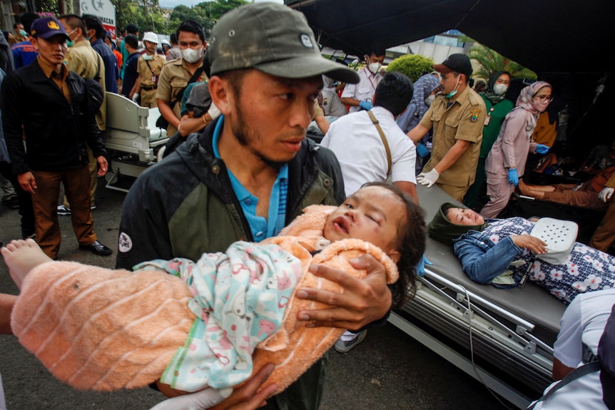 A man carries an injured child to receive treatment at a hospital, after an earthquake hit in Cianjur.