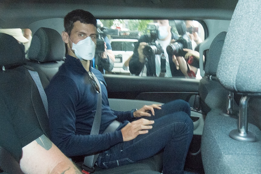 Novak Djokovic is seen sitting in the back seat of a car wearing street clothes and a facemask