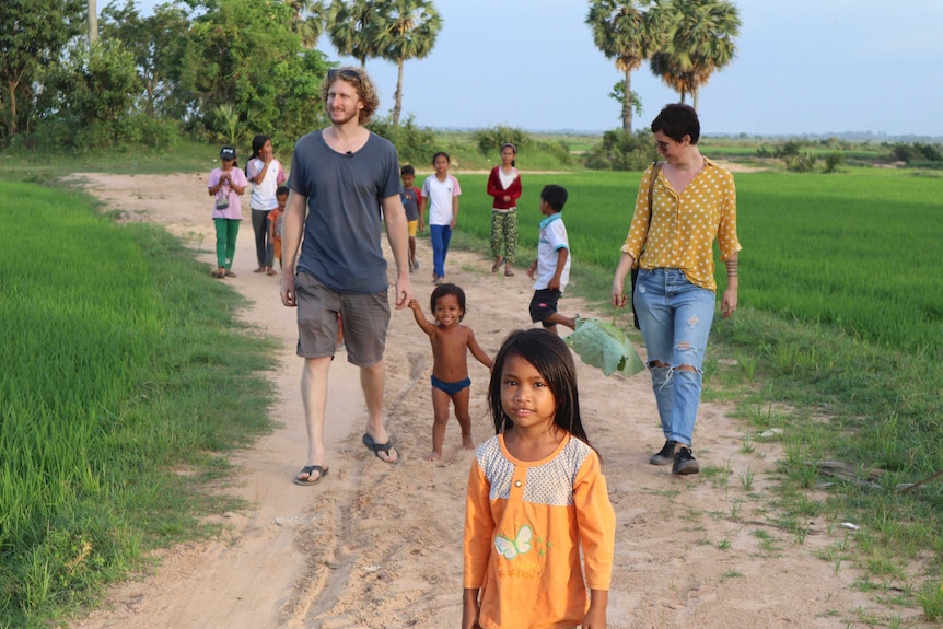 Two Australians walk with children in a grassy part of a Cambodian village