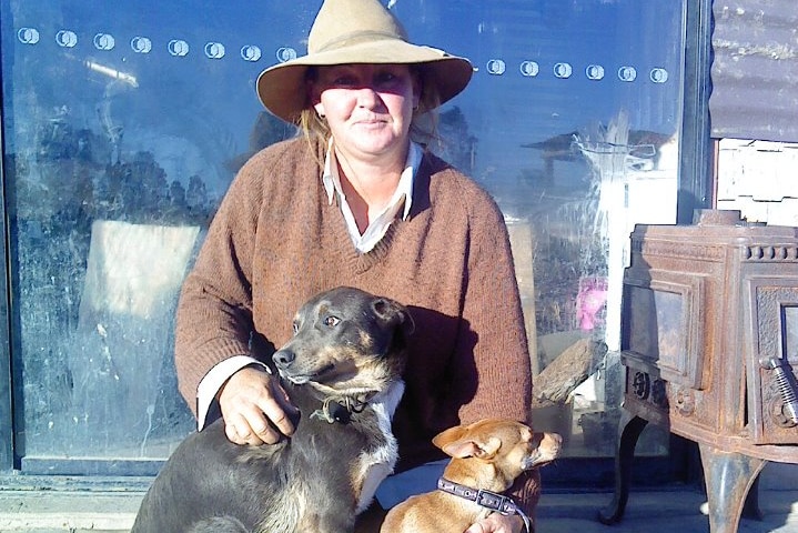 Queensland drover Jen McClelland kneeling with two dogs with a hat on