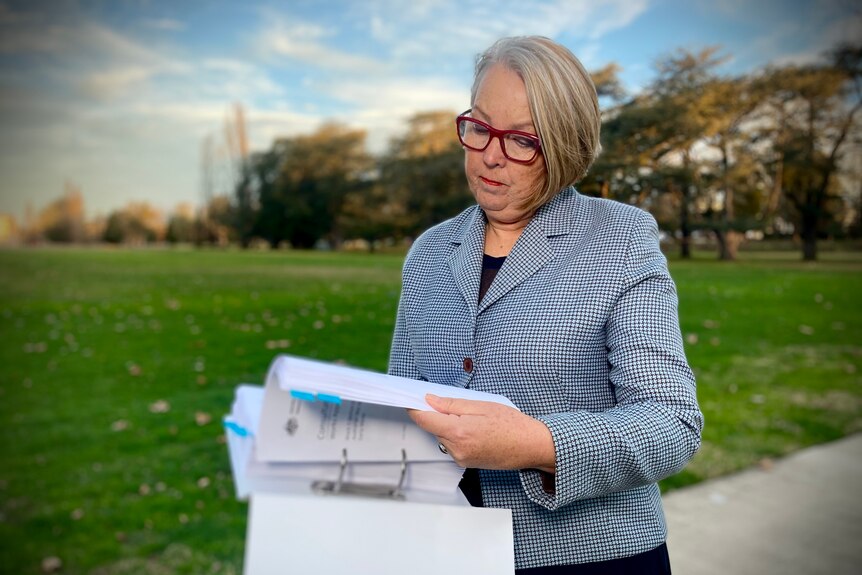 Woman wearing a suit jacket and glasses looks at various pages in a park.