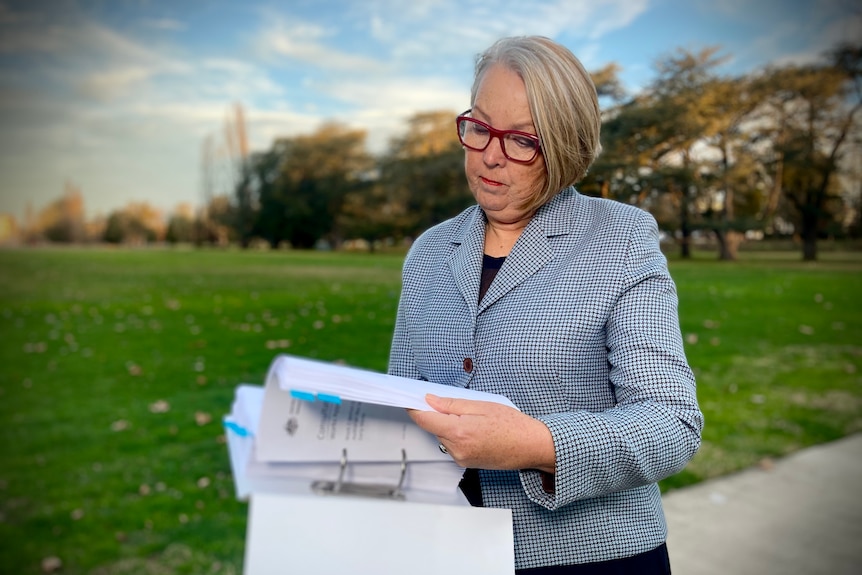 Woman wearing a suit jacket and glasses looks at various pages in a park.