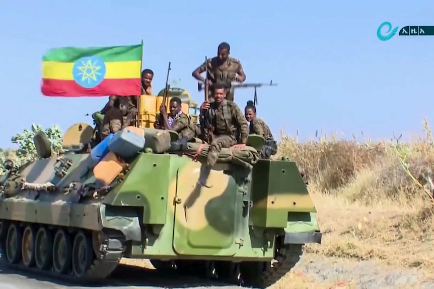 Ethiopian military sitting on an armoured personnel carrier next to a national flag