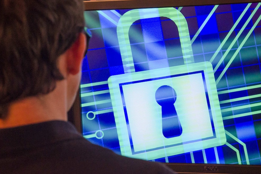 A man is looking at a computer scree displaying a padlock graphic