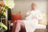 Brigitte Nielsen sitting on chair with one hand on pregnant stomach.