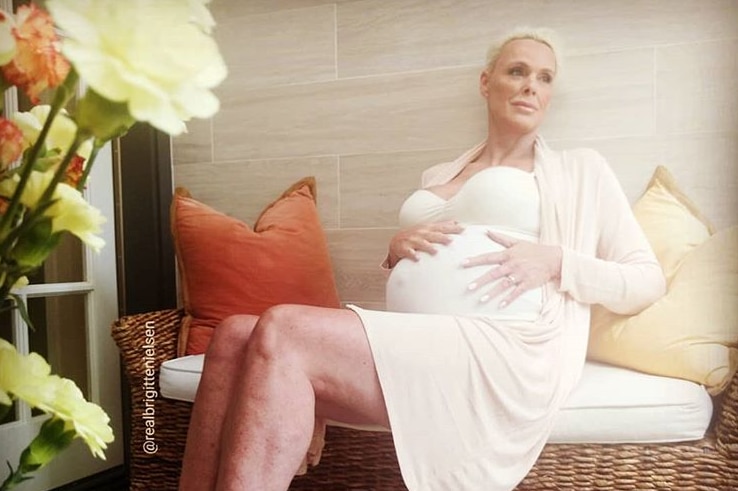 Brigitte Nielsen sitting on chair with one hand on pregnant stomach.