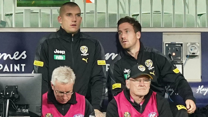 Two Richmond AFL players sit on the bench during a match against Melbourne.