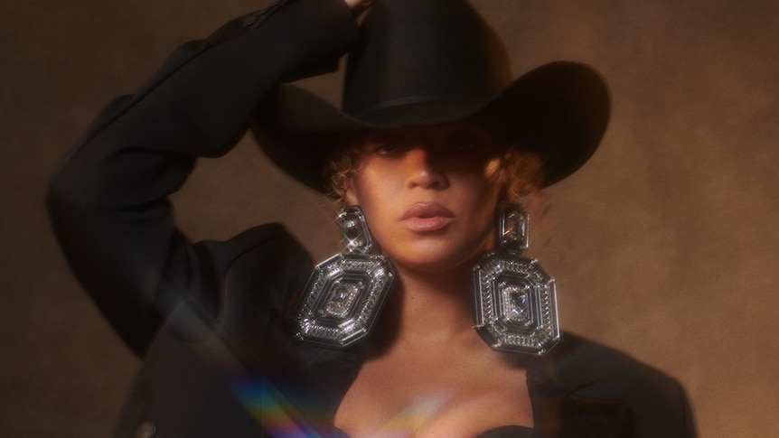 Beyonce wearing a black jacket, black cowboy hat, and big silver earrings