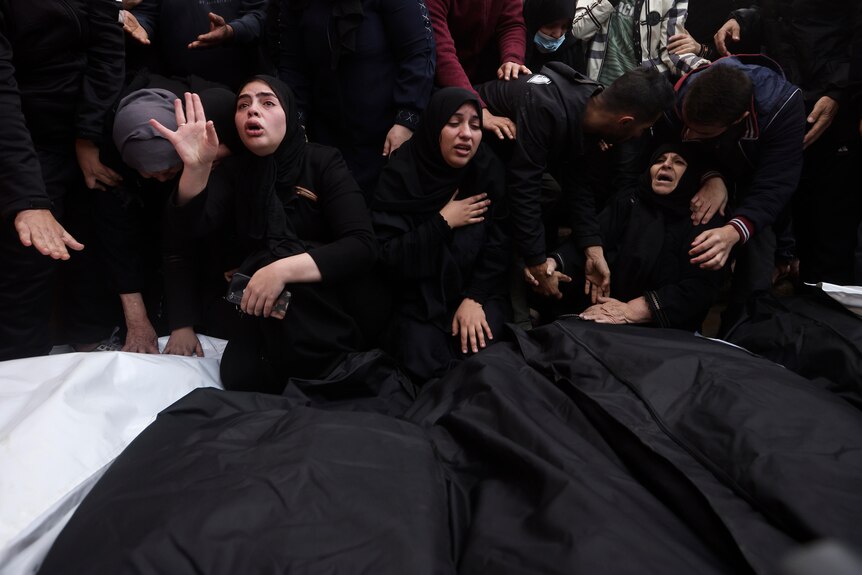 Women dressed all in black weep over black body bags. 