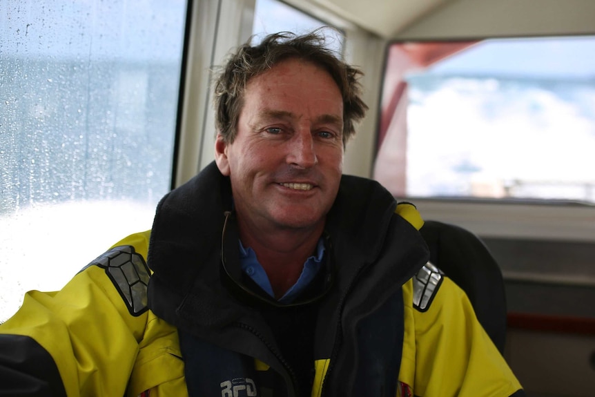 A man in a yellow and blue rain coat smiles while sitting on a ship.