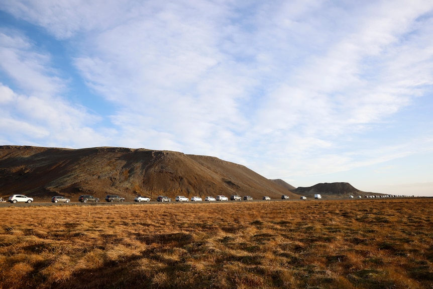 A line of cars is pictured from afar with a dry, vulanic looking landscape around it.