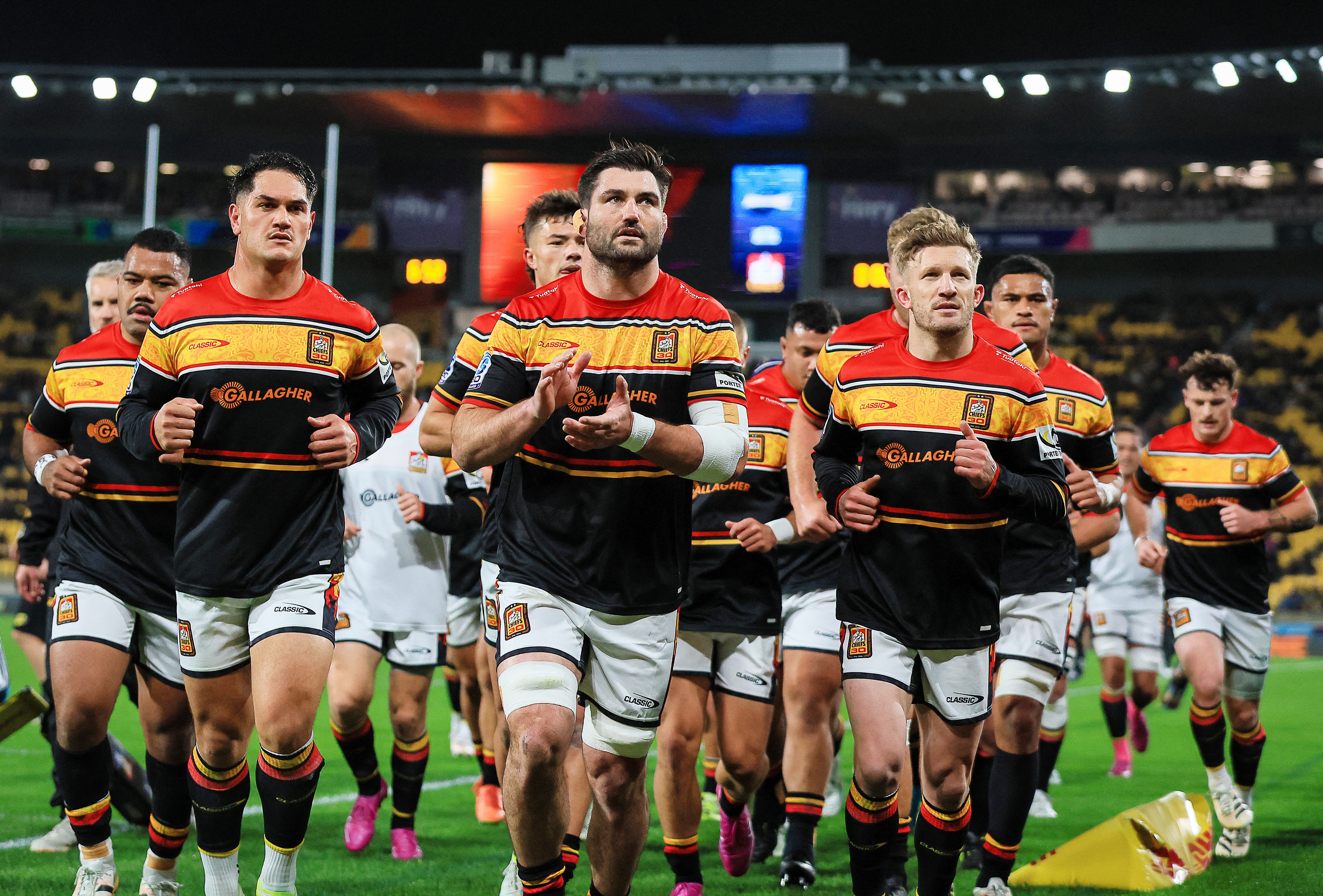 A team runs out onto a field in jerseys and shorts.