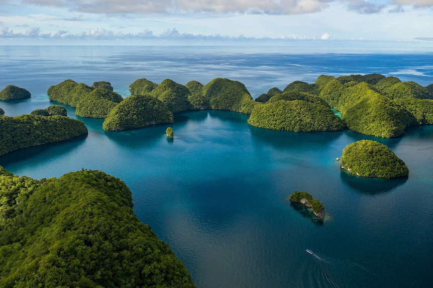 Aerial image of a series of lush green islands in a blue ocean. Clouds meet the horizon. 