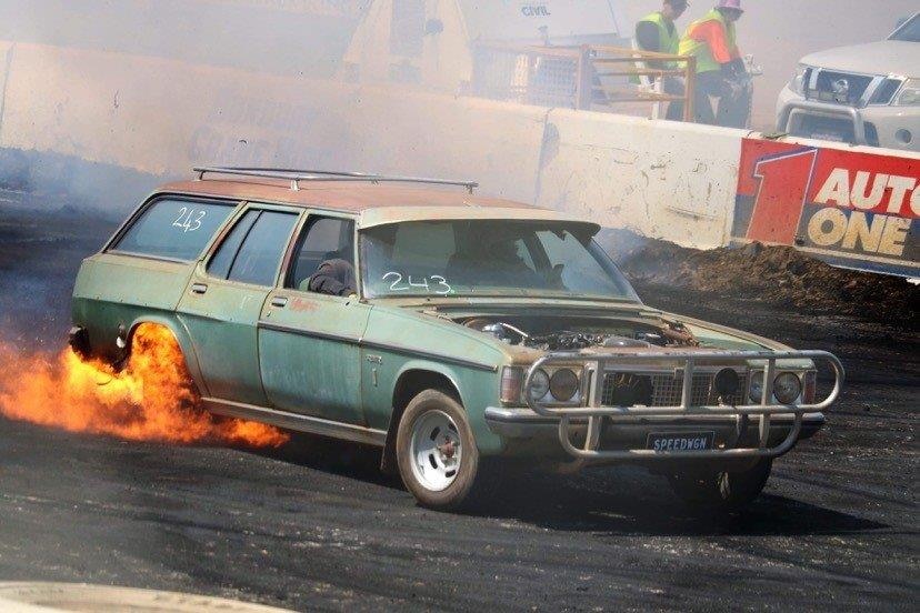 An old station wagon lays a fiery skid on a bitumen surface.