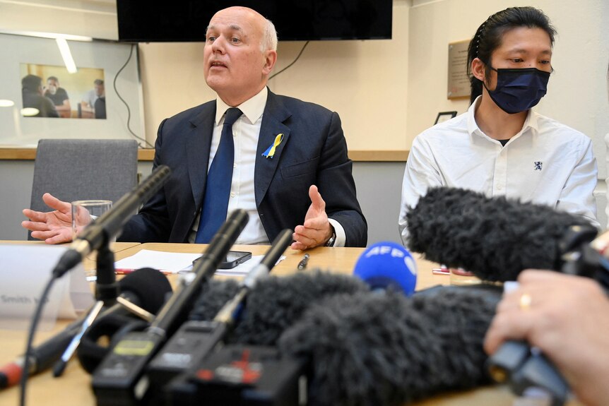British MP Iain Duncan Smith speaks during a news conference, while sat next to protester Bob Chan.