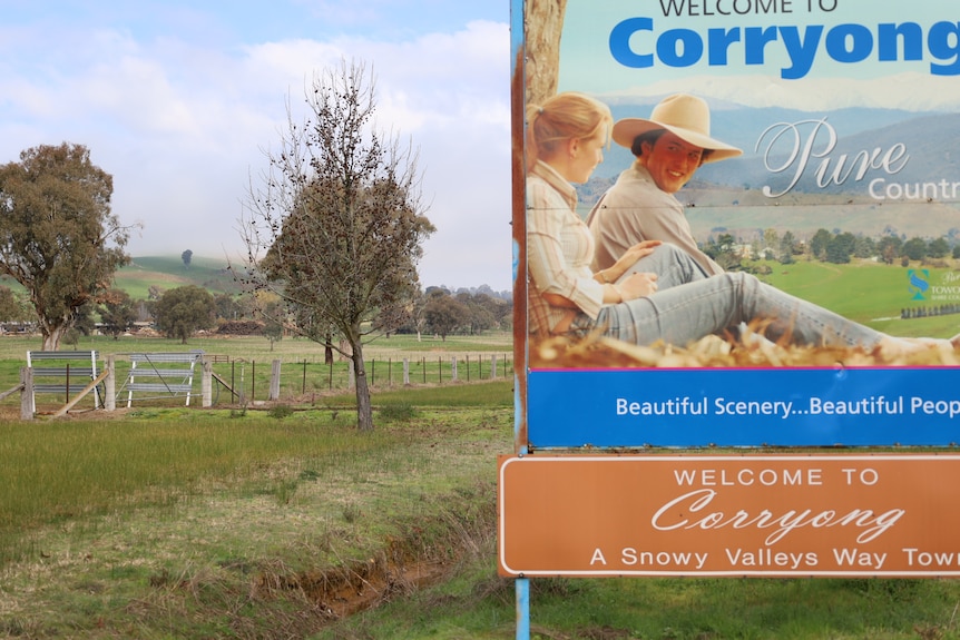 A saw mill sits in the distance behind sign welcoming drivers to the town of Corryong