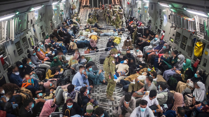 crowds of Afghanistan evacuees sitting on floor or side of an aircraft with defence force members also onboard.