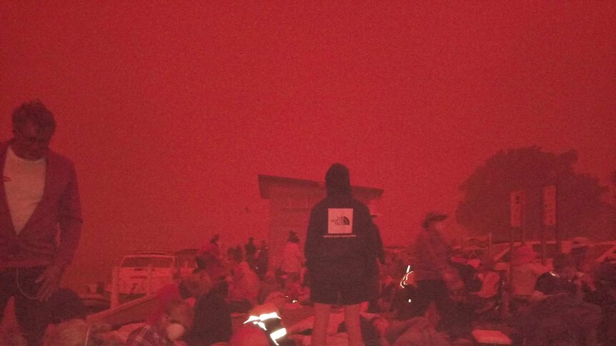 People gather on the Mallacoota boat ramp under a red haze.