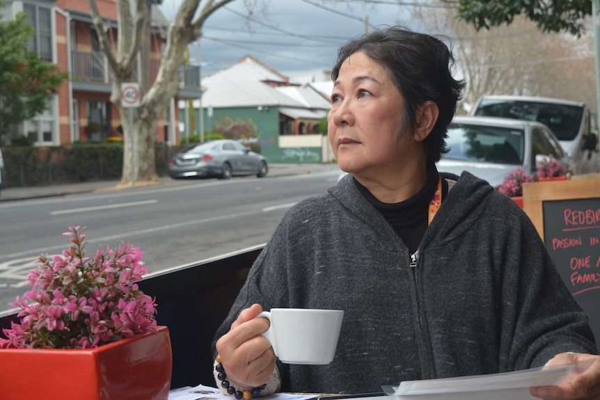 A woman holds a coffee and stares off into the distance on a Melbourne street with a grey sky.