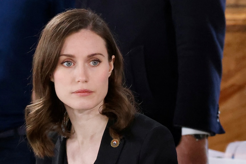 A tight portrait of Sanna Marin, looking thoughtful in a blue blazer with her hair flowing over her shoulders