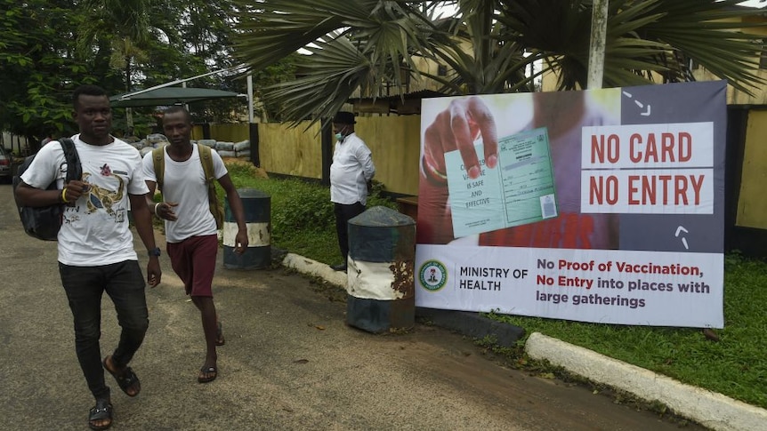 Two men in Nigeria walk past a sign saying No Vaccine Card, No Entry