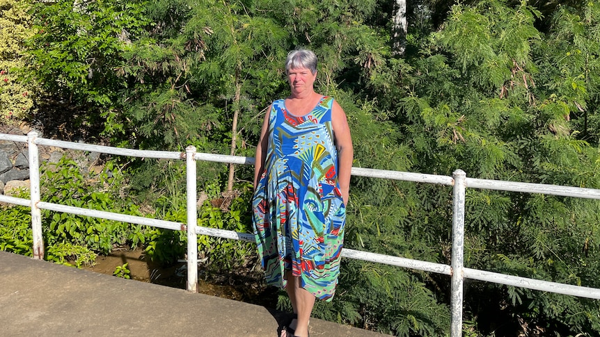 A woman in a colourful dress stands in front of trees.