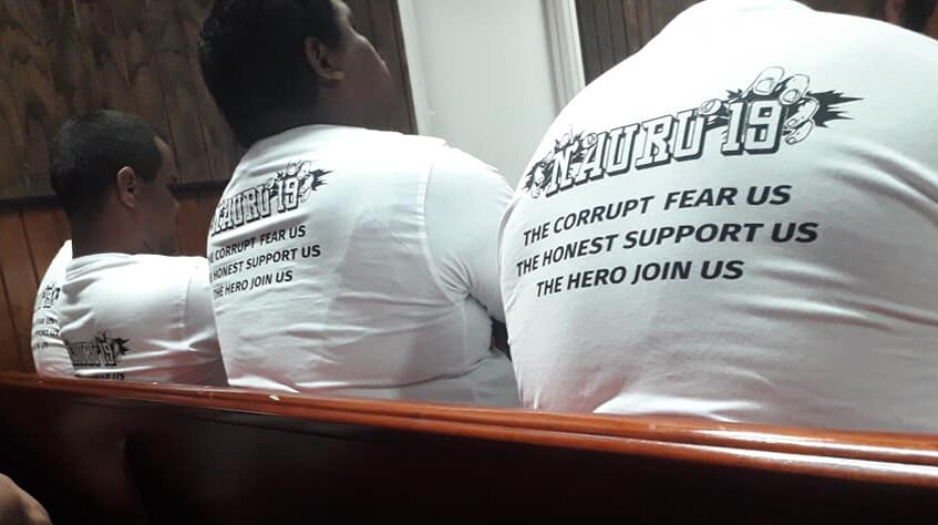 Members of the Nauru 19 sit in court wearing T-shirts that say 'the corrupt fear us, the honest support us, the hero join us'.