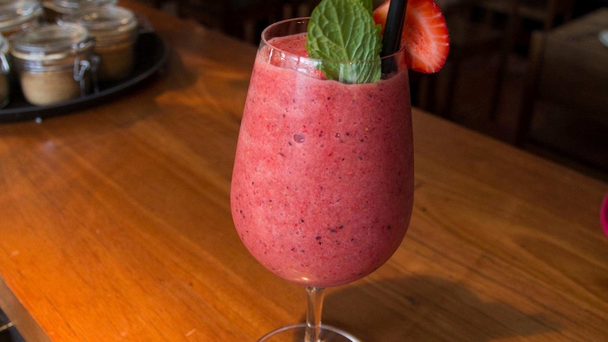 A wine glass of smoothie topped with mint and half a strawberry