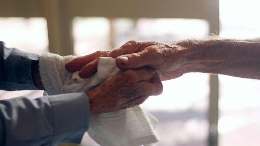 A woman holds a hand of an old mans