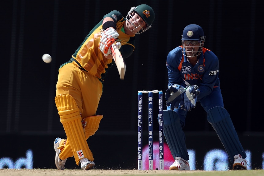 An Indian wicketkeeper watches as an Australian batsman crashes the ball toward the fence for six during a T20 World Cup match.