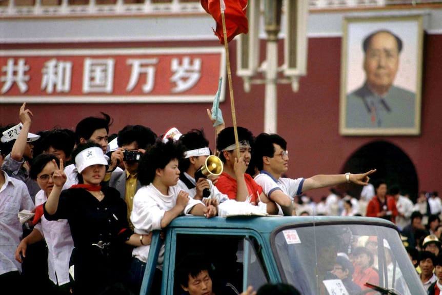 Student protesters arriving at Tiananmen Square ride past a portrait of Mao, they are riding in a ute or truck