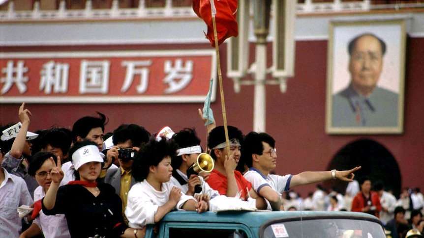 Student protesters arriving at Tiananmen Square ride past a portrait of Mao, they are riding in a ute or truck