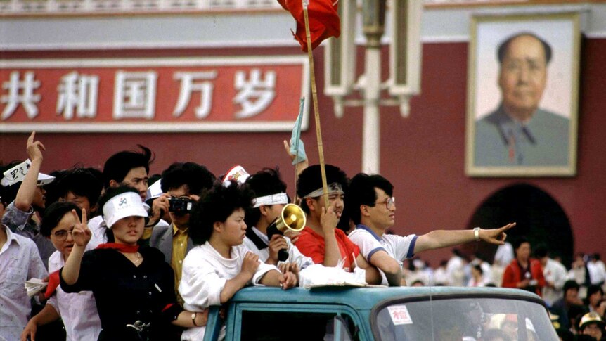 A group of young people in the back of a ute driving past a huge portrait of Chairman Mao