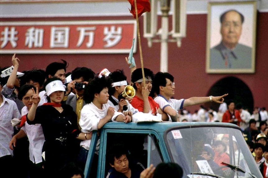 A group of young people in the back of a ute driving past a huge portrait of Chairman Mao