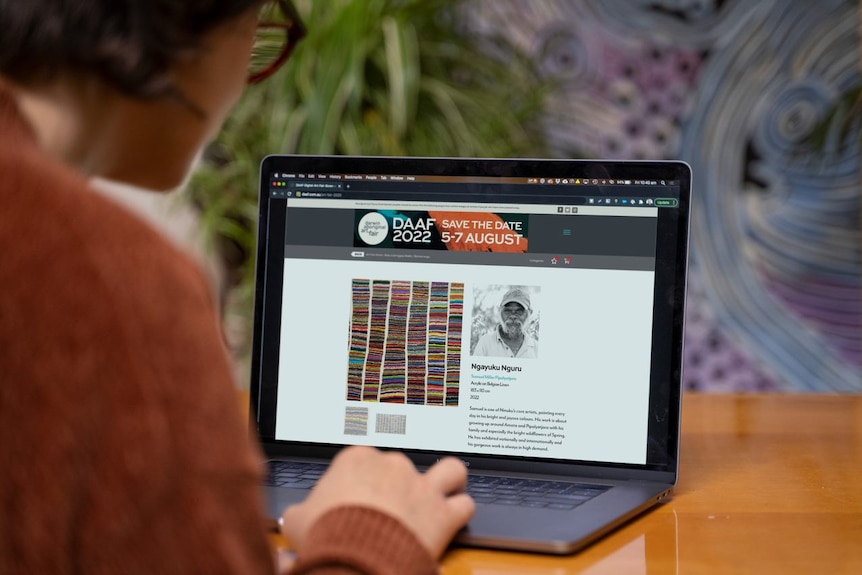 A shot over a person's shoulder as they browse the website of the Darwin Aboriginal Art Fair.