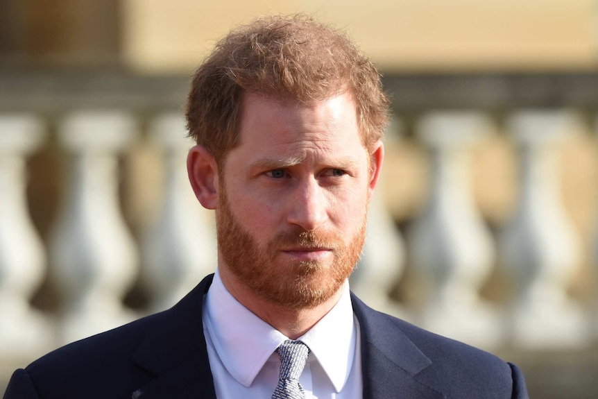 Prince Harry with a beard and furrowed brow wearing a suit and tie