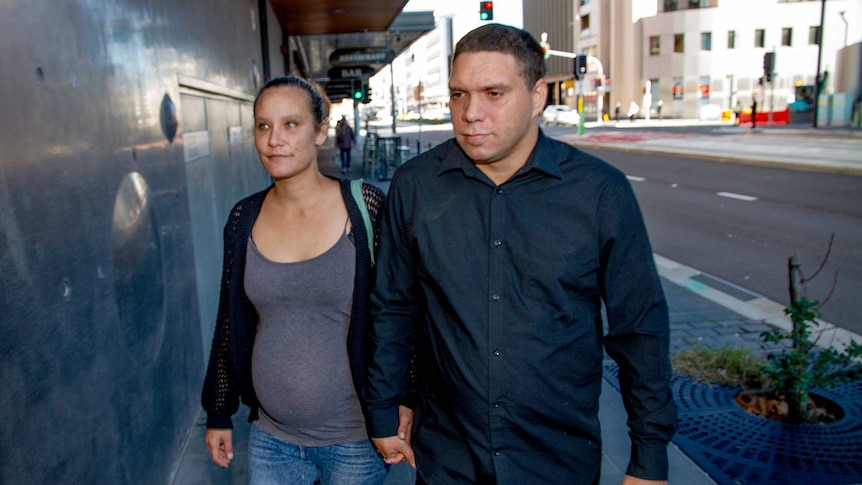 A woman and a man arrive at court holding hands.