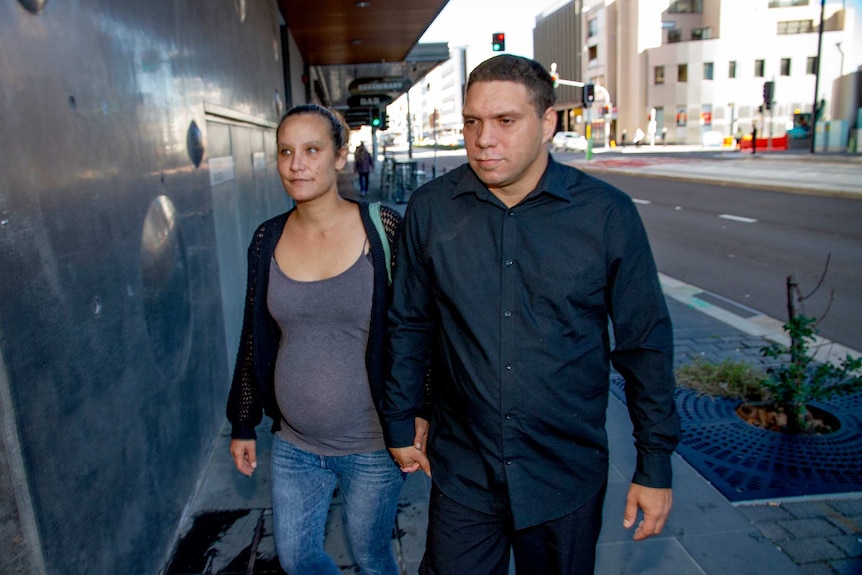 A woman and a man arrive at court holding hands.