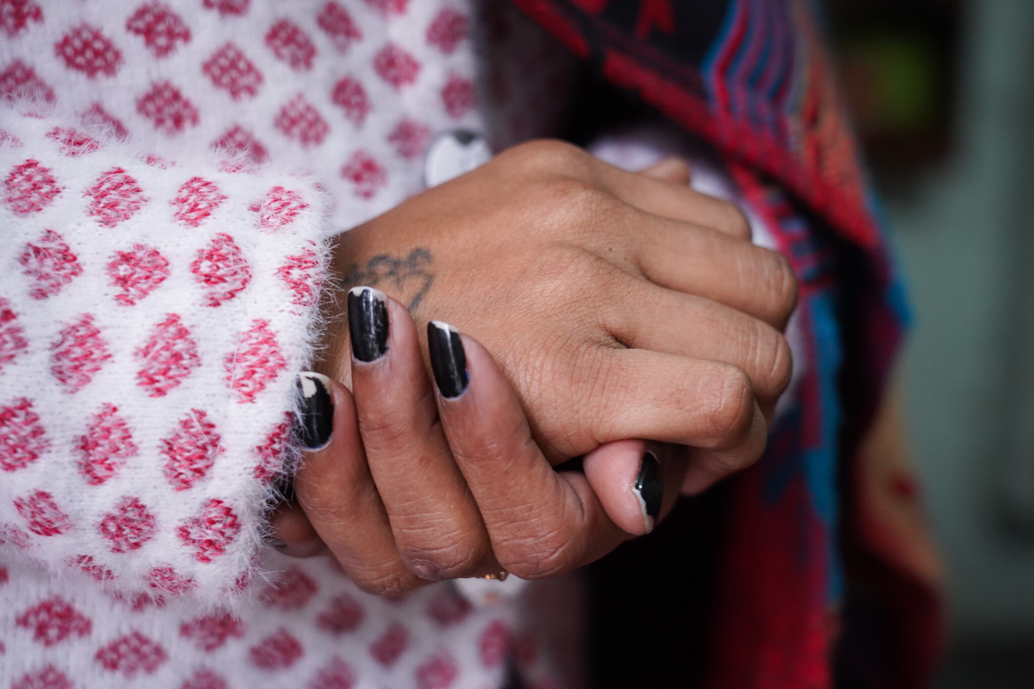 A woman clasps her hands together while wearing a pink and white coat.