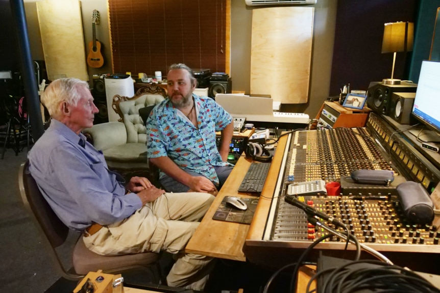 Two men sit chatting in a music studio.
