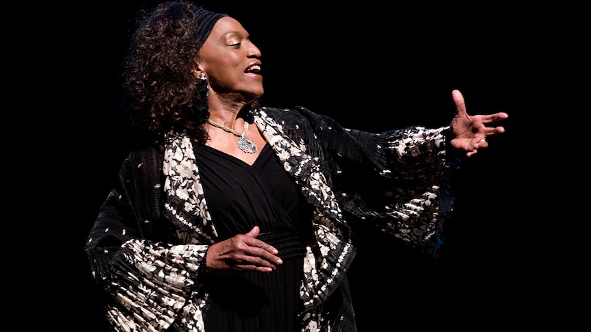 Opera singer Jessye Norman signing on stage with her arm outstretched in front of her.