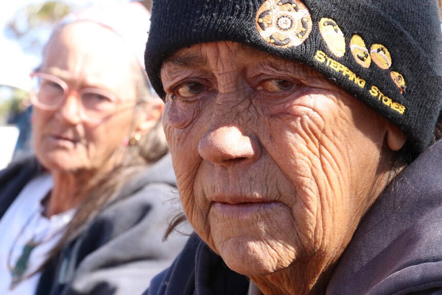 Close up of woman wearing black beanie looking at camera, another woman in background blurred, wearing glasses