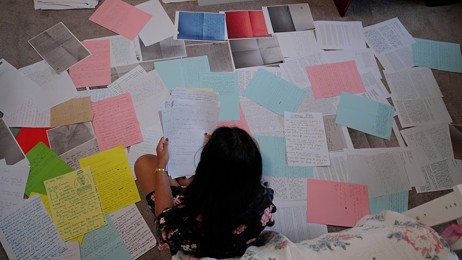 Una joven está sentada rodeada de cartas de jóvenes que han escrito al Primer Ministro.