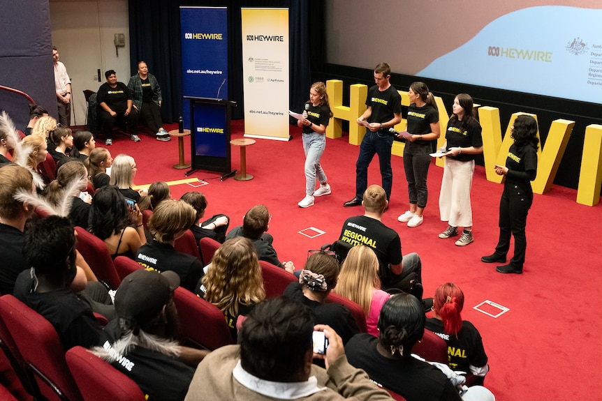 Five young people stand in front of an audience, presenting