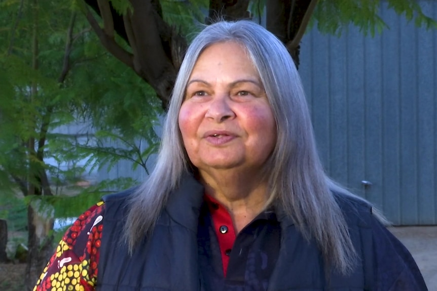 A woman with grey hair and Aboriginal artwork on her shirt.